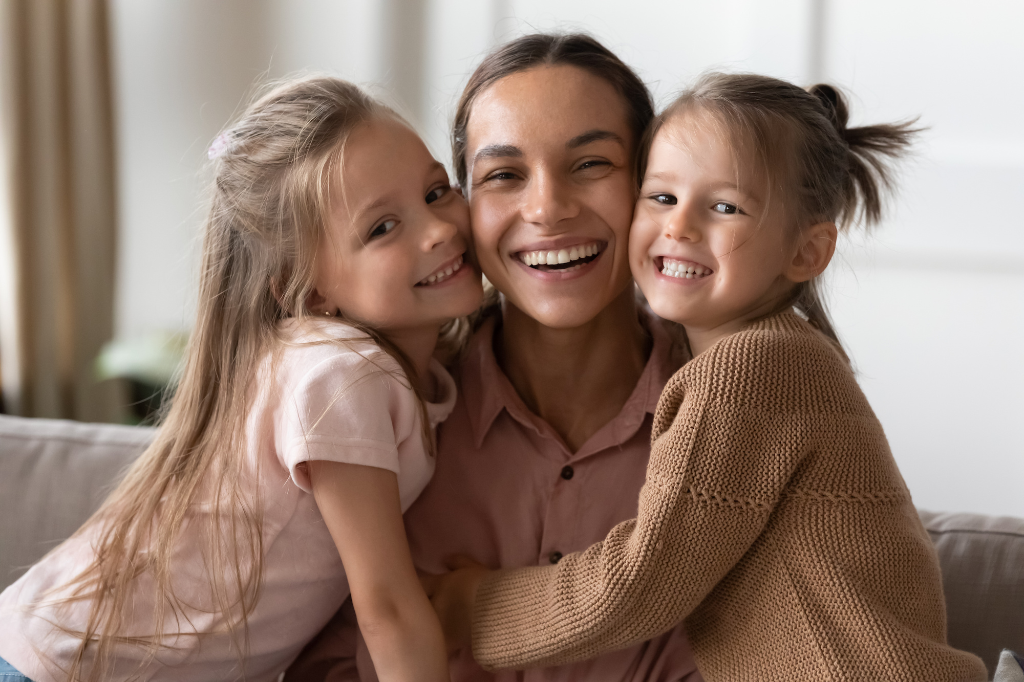 Happy mother and children daughters embracing looking at camera